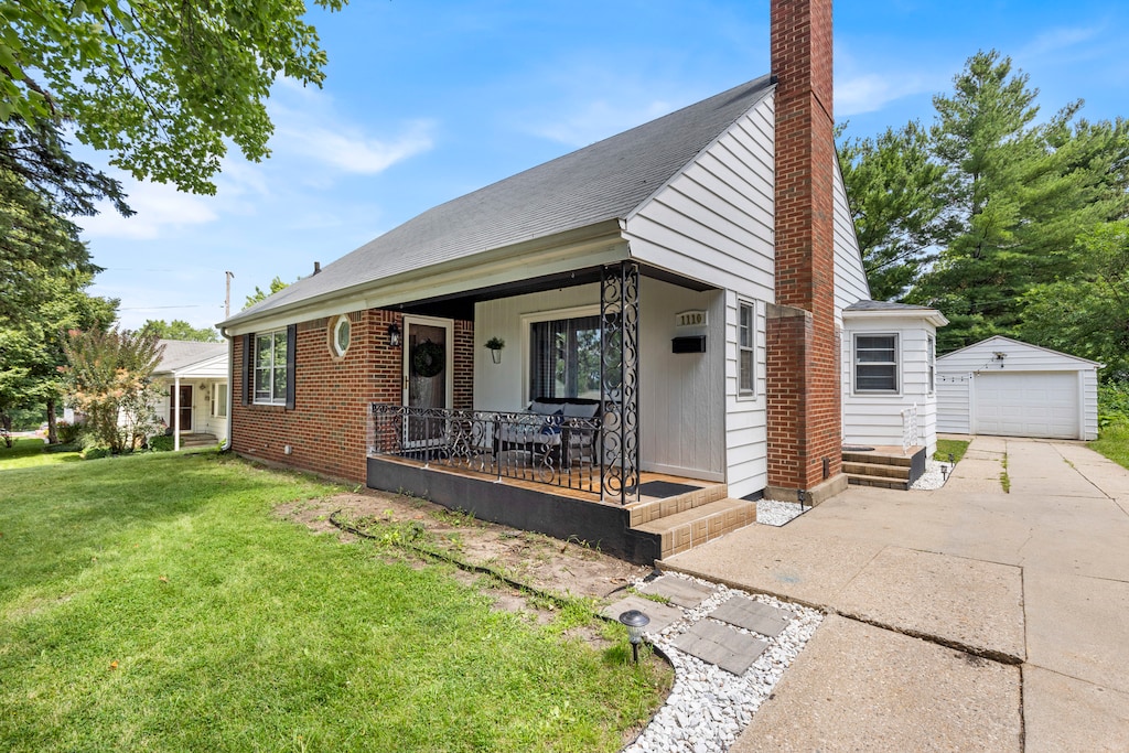 bungalow featuring a garage, covered porch, an outdoor structure, and a front lawn