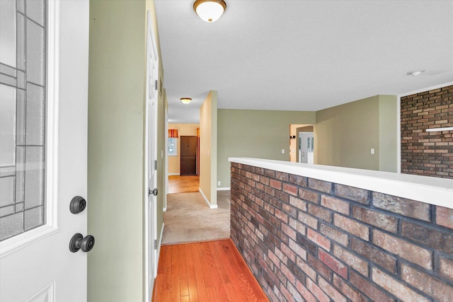 corridor featuring hardwood / wood-style floors, a textured ceiling, and brick wall