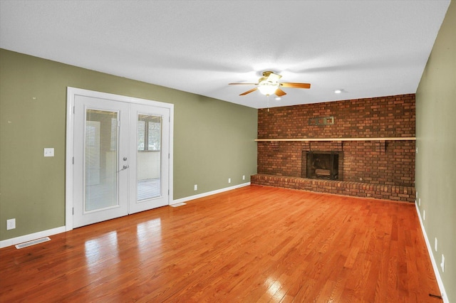 unfurnished living room featuring french doors, a brick fireplace, a textured ceiling, ceiling fan, and wood-type flooring