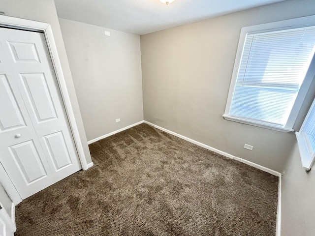 unfurnished bedroom with dark carpet and a closet