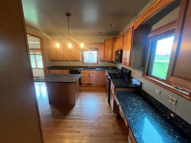 kitchen with sink, dark stone counters, decorative light fixtures, wood-type flooring, and black appliances