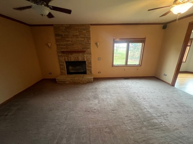 unfurnished living room featuring a stone fireplace, crown molding, carpet, and ceiling fan