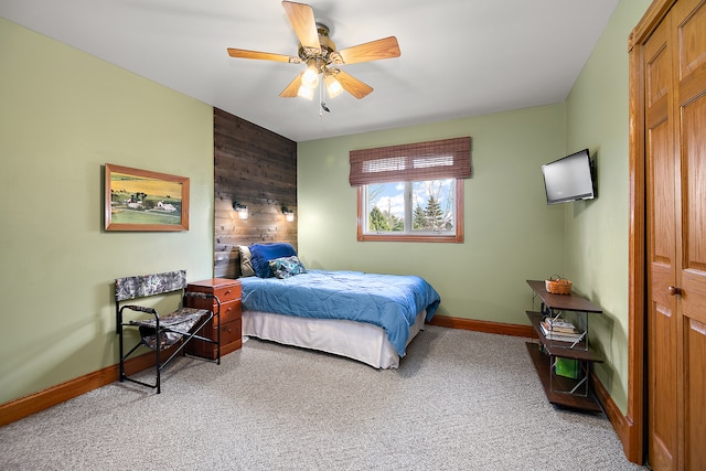 carpeted bedroom with ceiling fan, wood walls, and a closet