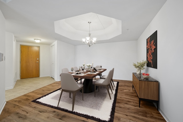 dining area with a chandelier, wood-type flooring, and a raised ceiling