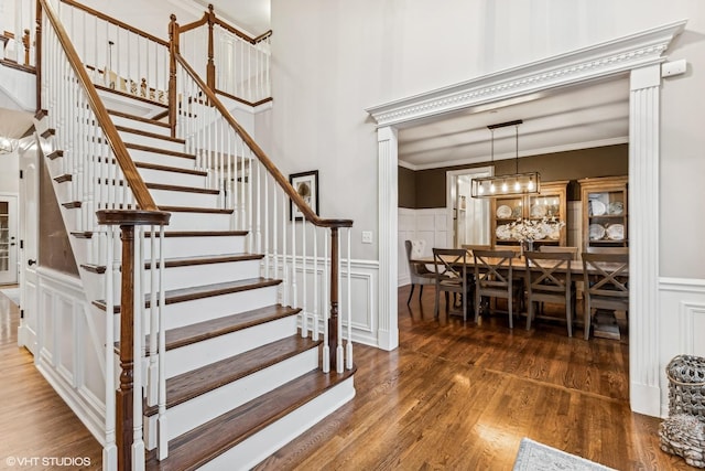 stairs featuring wood finished floors, a high ceiling, crown molding, a decorative wall, and a notable chandelier