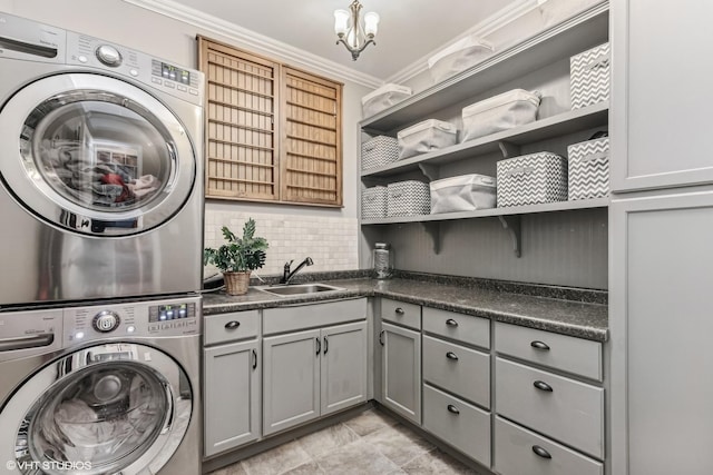 laundry room featuring cabinet space, stacked washer / drying machine, an inviting chandelier, crown molding, and a sink