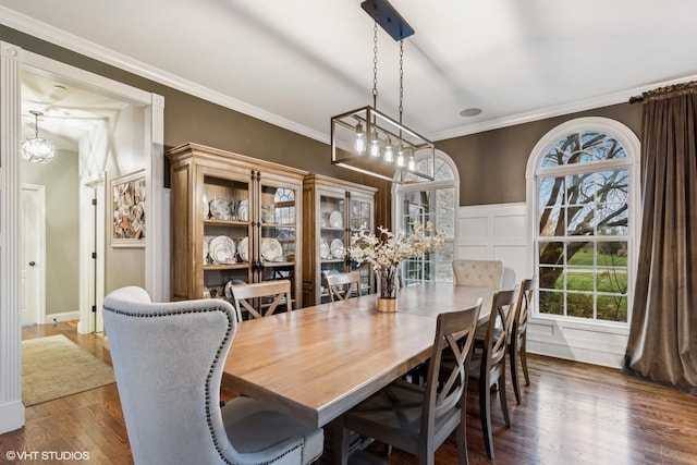 dining area featuring a wainscoted wall, a decorative wall, crown molding, and wood finished floors