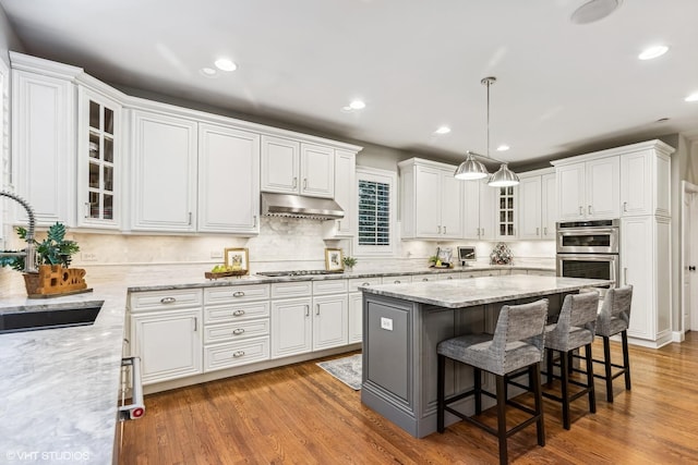 kitchen with under cabinet range hood, white cabinetry, stainless steel appliances, and a sink