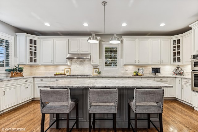 kitchen featuring a breakfast bar area, a center island, white cabinets, and under cabinet range hood