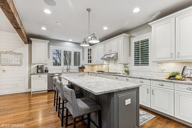 kitchen featuring appliances with stainless steel finishes, white cabinetry, under cabinet range hood, and a kitchen bar