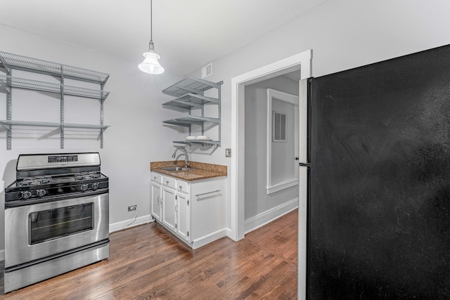 kitchen featuring hanging light fixtures, stainless steel gas range, black fridge, dark hardwood / wood-style floors, and white cabinets