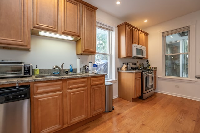 kitchen with dark stone counters, stainless steel appliances, light hardwood / wood-style floors, and sink