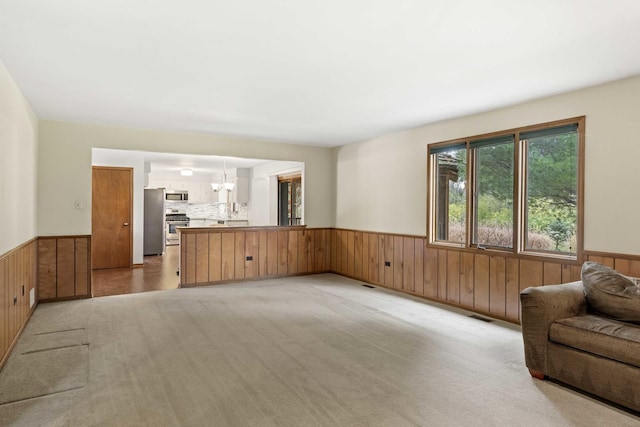 unfurnished living room featuring wood walls, light colored carpet, and a chandelier