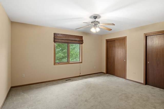 unfurnished bedroom with light carpet, two closets, and ceiling fan