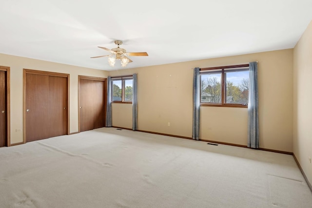 unfurnished bedroom featuring two closets, ceiling fan, and light colored carpet