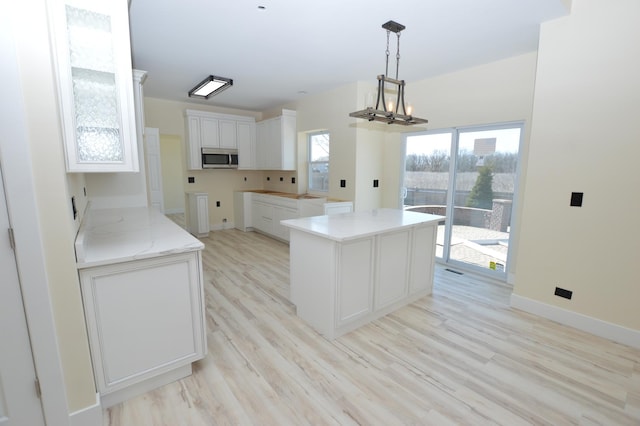 kitchen with baseboards, light wood finished floors, white cabinets, stainless steel microwave, and a chandelier