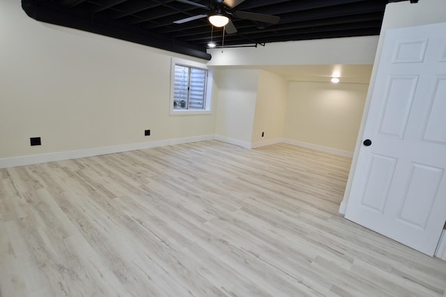 below grade area with baseboards, light wood-style flooring, and a ceiling fan