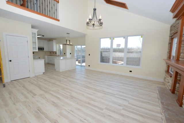 unfurnished living room featuring light wood-style flooring, baseboards, high vaulted ceiling, and a chandelier