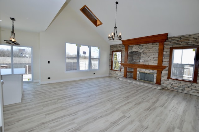 unfurnished living room with baseboards, high vaulted ceiling, a stone fireplace, a notable chandelier, and light wood-type flooring