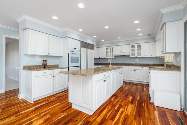 kitchen featuring white oven, a kitchen island with sink, white cabinets, and dark hardwood / wood-style floors