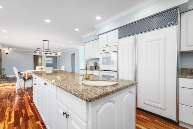 kitchen with white cabinets, dark hardwood / wood-style flooring, an island with sink, and hanging light fixtures