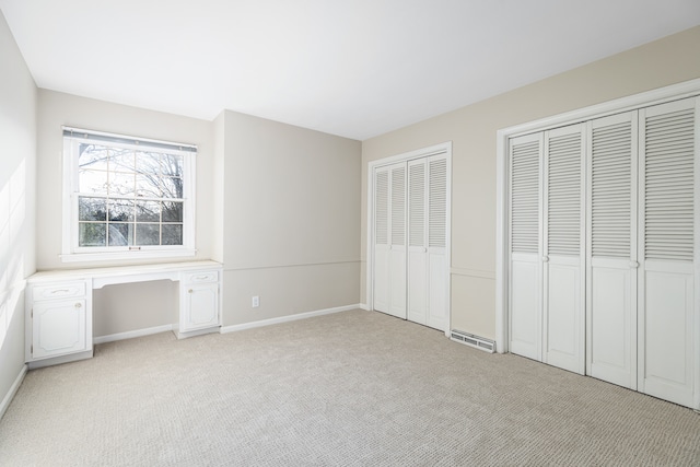 unfurnished bedroom with light carpet, built in desk, and multiple closets