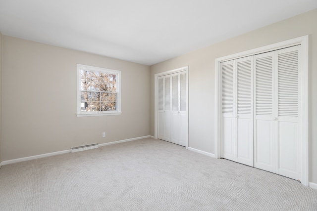 unfurnished bedroom featuring light carpet and two closets