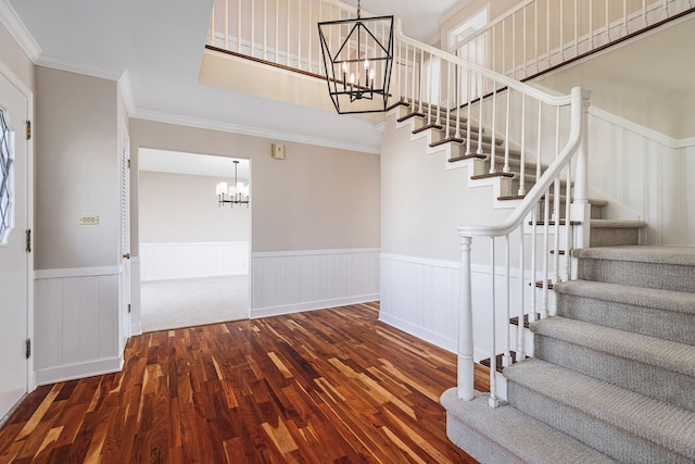 stairway with wood-type flooring, an inviting chandelier, and crown molding