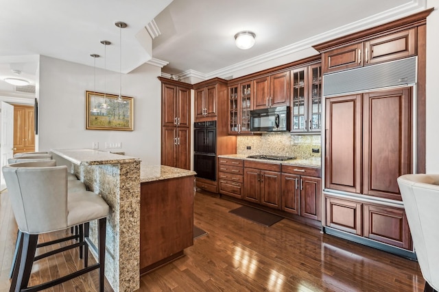 kitchen with light stone countertops, hanging light fixtures, a kitchen island, black appliances, and ornamental molding