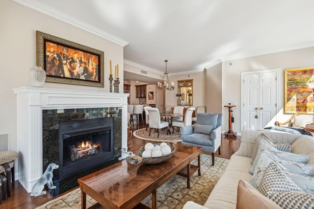 living room featuring a tiled fireplace, crown molding, an inviting chandelier, and light wood-type flooring