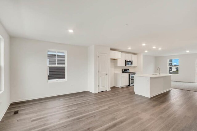 kitchen featuring white cabinets, sink, light wood-type flooring, an island with sink, and appliances with stainless steel finishes