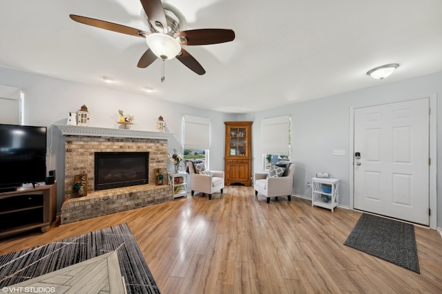 living room featuring a fireplace, light wood-type flooring, and ceiling fan