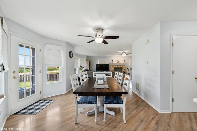 dining space featuring ceiling fan, light wood-type flooring, and a fireplace