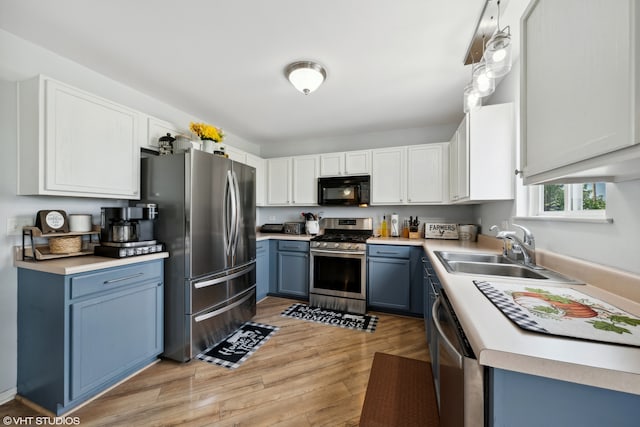 kitchen featuring appliances with stainless steel finishes, light wood-type flooring, sink, blue cabinetry, and white cabinets