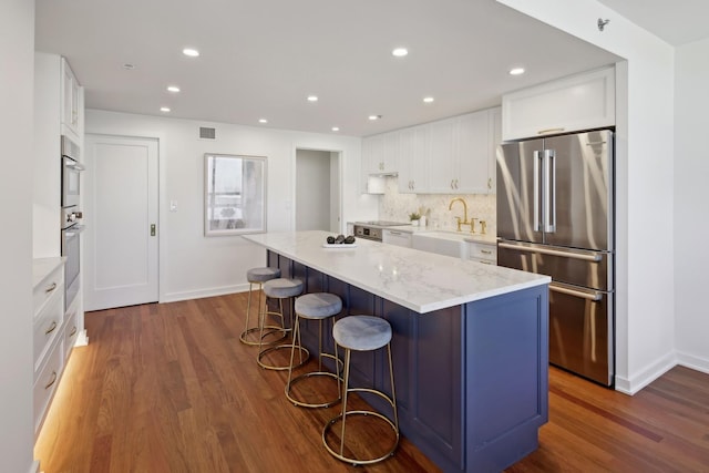 kitchen featuring dark wood-style floors, a center island, appliances with stainless steel finishes, white cabinets, and a kitchen bar