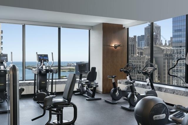 workout area with floor to ceiling windows, a water view, and a city view