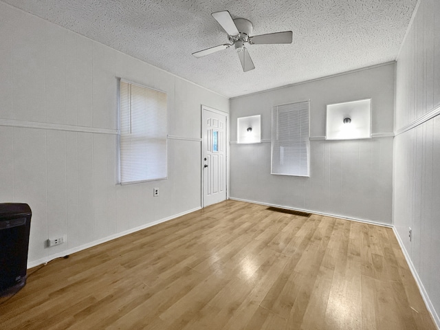 unfurnished living room with ceiling fan, wooden walls, light hardwood / wood-style floors, and a textured ceiling