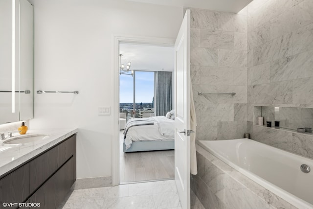 bathroom featuring a chandelier, vanity, and tiled bath