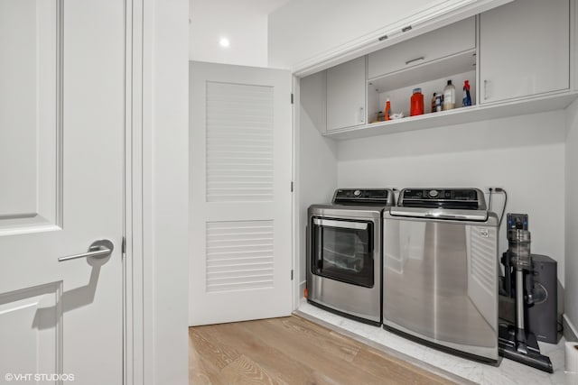 laundry area with cabinets, light hardwood / wood-style flooring, and washing machine and clothes dryer