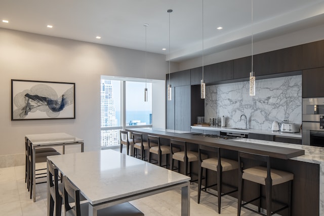 kitchen featuring pendant lighting, a breakfast bar, a center island, sink, and light stone countertops