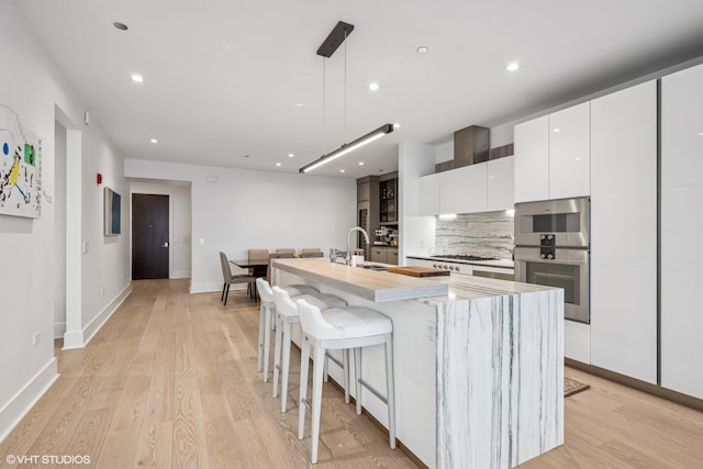 kitchen featuring light wood-type flooring, stainless steel appliances, sink, a center island with sink, and white cabinets