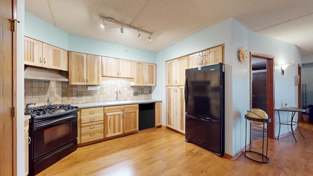 kitchen featuring light brown cabinets, a sink, under cabinet range hood, and black appliances