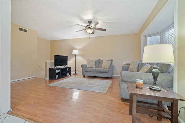 living room featuring a textured ceiling, light wood-type flooring, and ceiling fan