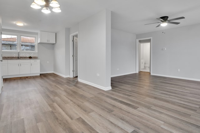 unfurnished living room featuring sink, light hardwood / wood-style floors, and ceiling fan with notable chandelier