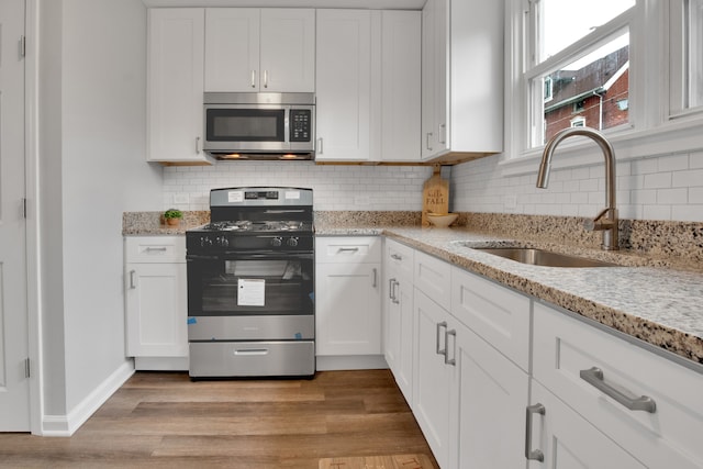 kitchen featuring light stone countertops, white cabinetry, sink, stainless steel appliances, and light hardwood / wood-style floors