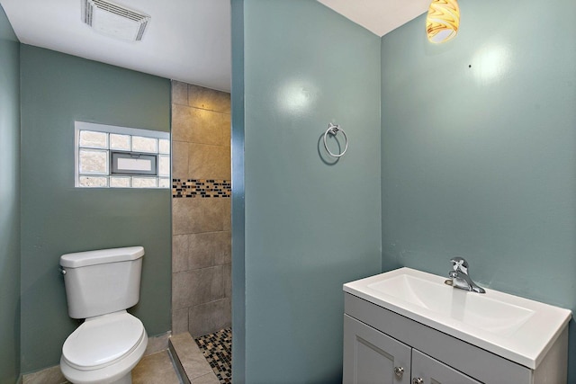 bathroom with tile patterned flooring, a tile shower, vanity, and toilet