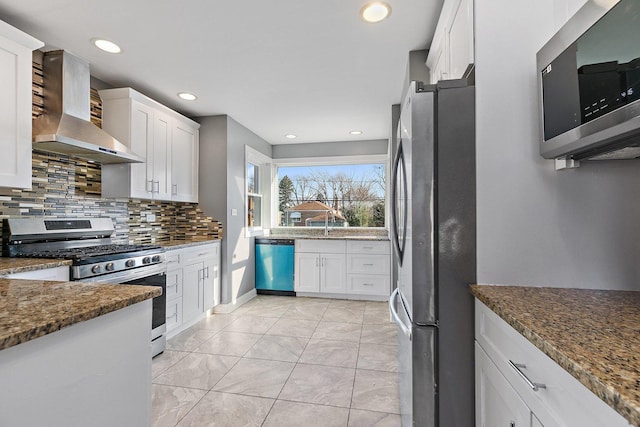 kitchen featuring white cabinetry, wall chimney range hood, appliances with stainless steel finishes, and dark stone counters