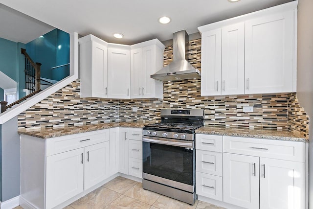 kitchen with backsplash, wall chimney exhaust hood, stainless steel gas range, stone counters, and white cabinets