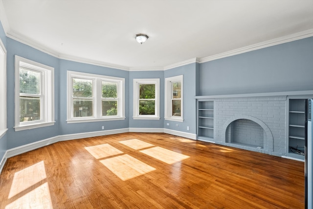 unfurnished living room with wood-type flooring, a brick fireplace, built in shelves, and crown molding