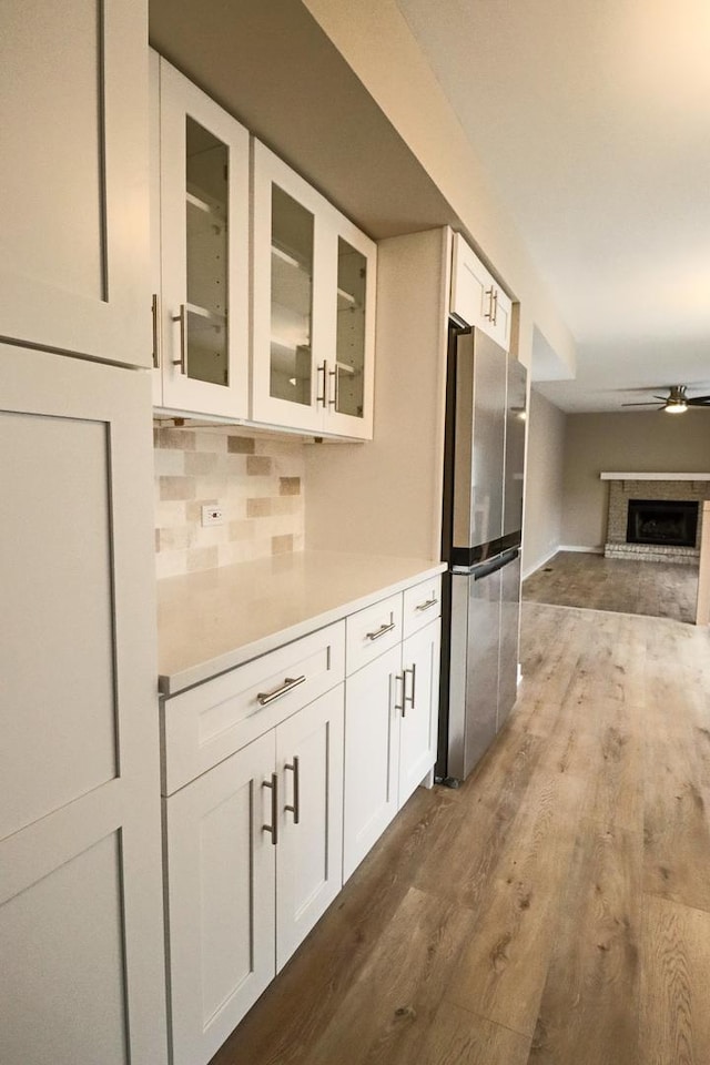 kitchen with stainless steel refrigerator, backsplash, white cabinets, hardwood / wood-style flooring, and ceiling fan